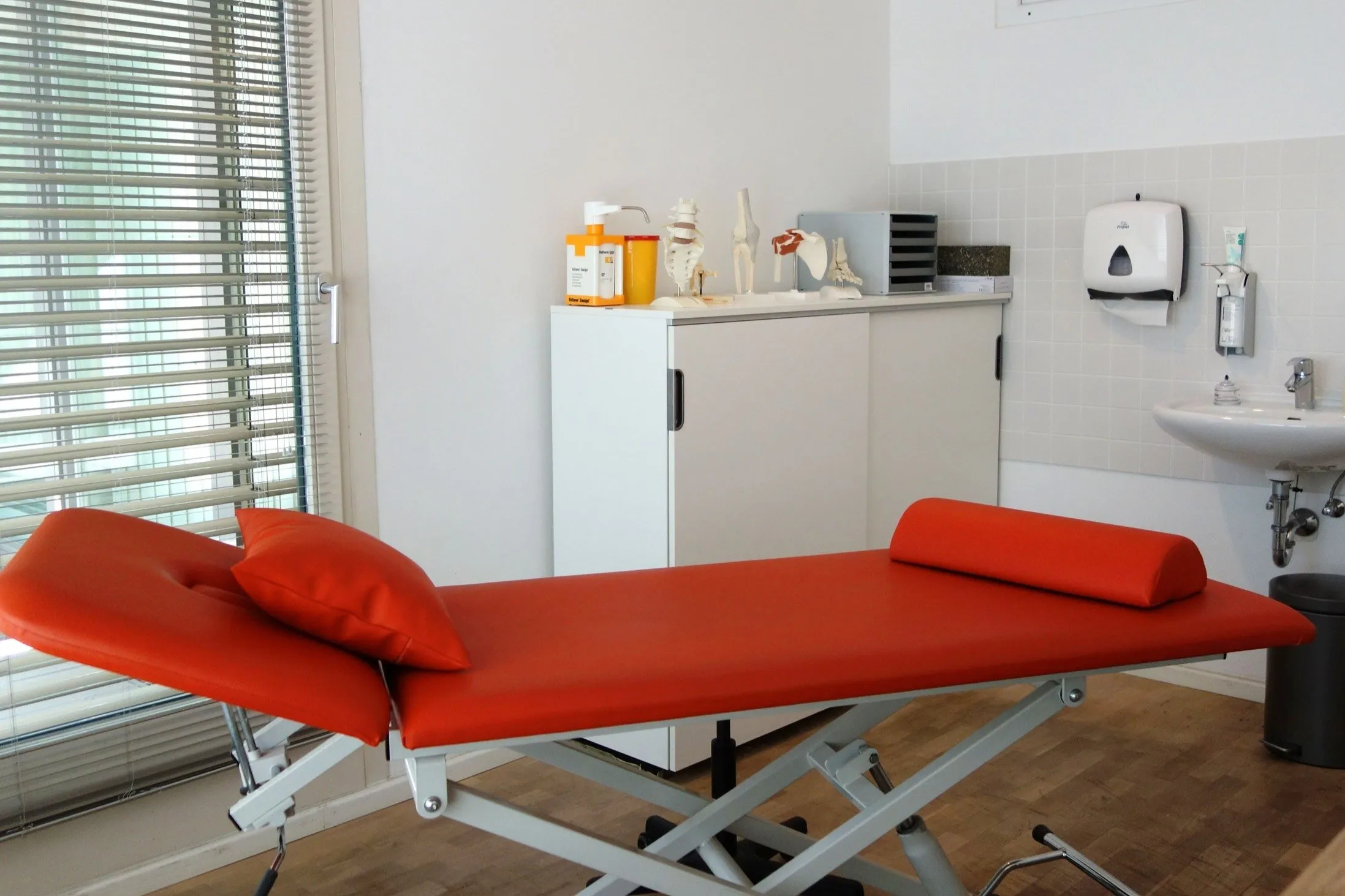 Heller Behandlungsraum mit orangefarbener Behandlungsliege