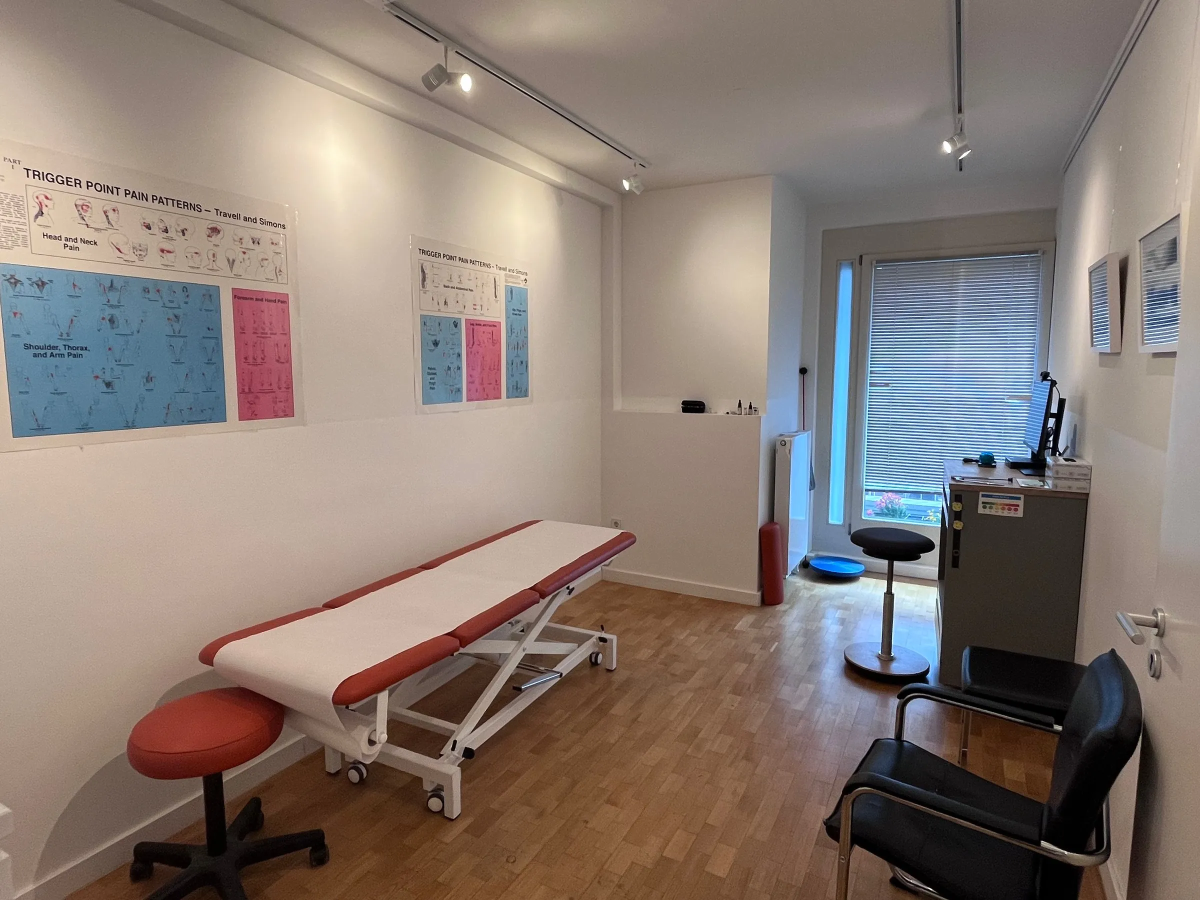 Behandlungsraum mit Liege und anatomischen Lehrtafeln