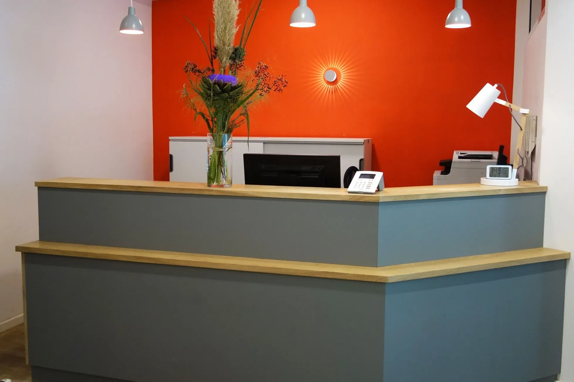 Empfangstresen der Orthopädischen Praxis Mitte vor orangefarbener Wand