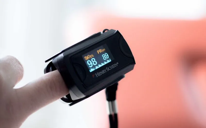 Pulsoximeter am Finger zeigt Sauerstoffsättigung und Pulsfrequenz an
